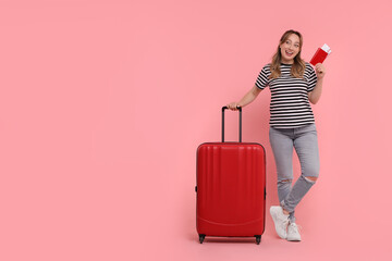 Happy young woman with passport, ticket and suitcase on pink background, space for text