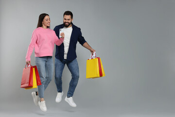 Happy couple with shopping bags and smartphone jumping on grey background. Space for text