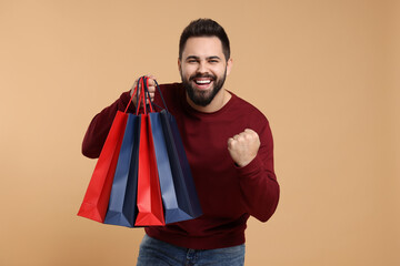 Happy man with many paper shopping bags on beige background