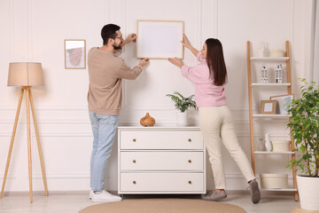 Man and woman hanging picture frame on white wall at home