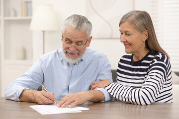 Happy senior couple signing Last Will and Testament indoors