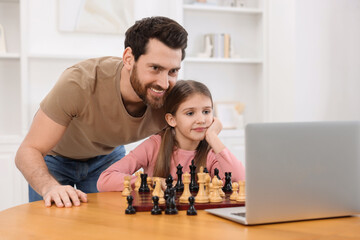 Father teaching his daughter to play chess following online lesson at home