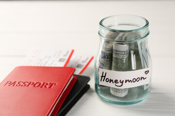 Glass jar with word Honeymoon, dollar banknotes, passports and plane tickets on white wooden table,...