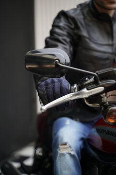 Closeup of a biker on a motorcycle, wearing leather & denim gloves, and leather jacket 