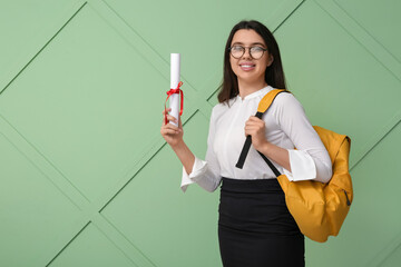 Happy smiling female student with diploma and backpack on green wooden background