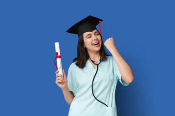 Happy female medical student in graduation hat with diploma on blue background