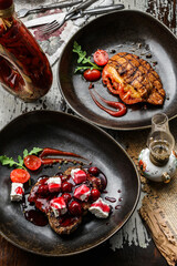 Grilled meat chop steaks with berries sauce, cheese and tomatoes on plate on wooden background. Meat Dishes, top view