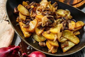 Fried homemade potatoes with mushrooms on plate on wooden background, top view
