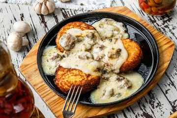 Fried potato pancakes with mushrooms creamy sauce in plate on wooden background. Homemade food, top view