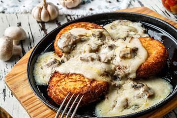 Fried potato pancakes with mushrooms creamy sauce in plate on wooden background. Homemade food, top view