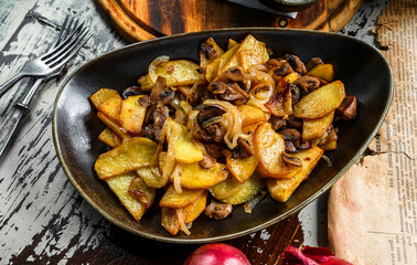 Fried homemade potatoes with mushrooms on plate on wooden background, top view