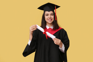 Happy female graduating student with diploma on yellow background