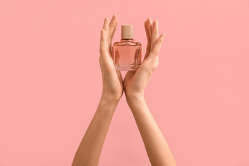 Female hands holding glass bottle of perfume on color background