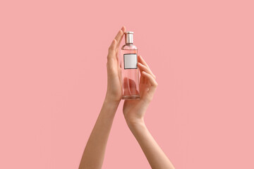 Female hands holding glass bottle of perfume on color background