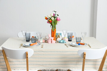 Beautiful table setting for Easter decorated with bouquet of carrots and flowers against white wall