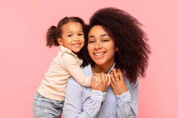 Happy black mother posing with her cute little daughter, girl hugging mom from back and smiling...