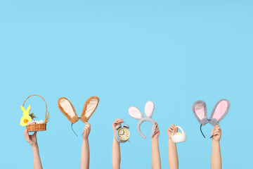 Female hands holding Easter bunny ears headbands with basket and alarm clock on blue background