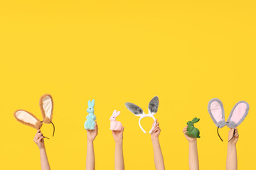 Female hands holding Easter bunny ears headbands and toy rabbits on yellow background