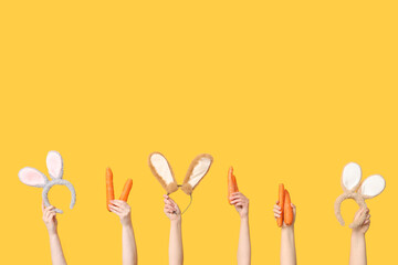 Female hands holding Easter bunny ears headbands and carrots on yellow background
