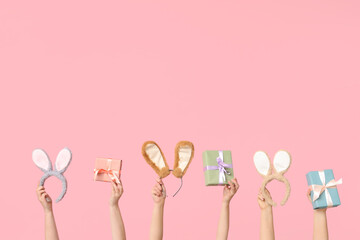 Female hands holding Easter bunny ears headbands and gift boxes on pink background