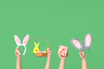 Female hands holding Easter bunny ears headbands with gift box and basket on green background