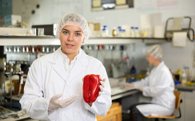 Positive young woman scientist biologist posing in the laboratory with red pepper in her hands