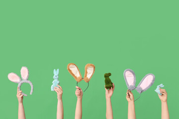 Female hands holding Easter bunny ears headbands and toy rabbits on green background