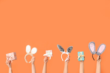 Female hands holding Easter bunny ears headbands and gift boxes on orange background