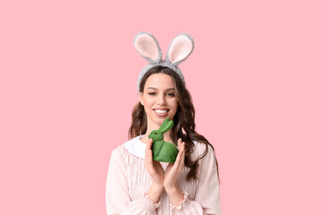 Happy young woman in Easter bunny ears headband with toy rabbit on pink background