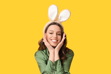 Happy young woman in Easter bunny ears headband on yellow background