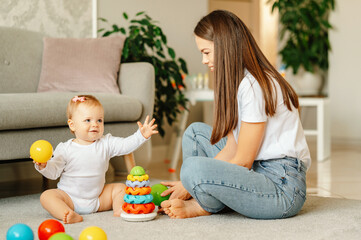 Naklejka premium Cute baby girl is playing with her mother and colourful toys on the floor at home.