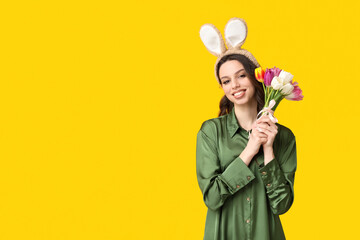 Happy young woman in Easter bunny ears headband with bouquet of tulips on yellow background
