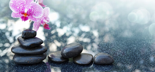 Black spa stone and pink orchid flowers on the gray table background.