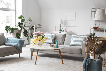 Interior of modern living room with flowers, Easter eggs and greeting card on coffee table