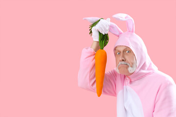 Senior man in Easter bunny costume with plush carrot on pink background