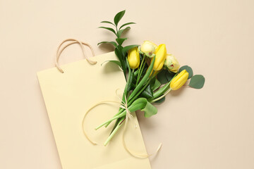 Paper shopping bag with yellow flowers and green twigs on beige background