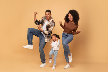 Excited african american family of three shaking clenched fists, making winner gesture, celebrating...