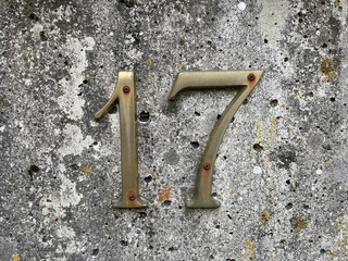 number 17 made of metal against the background of an old stone wall
