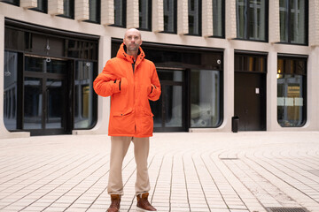 young positive man 30-35 years old man in bright orange jacket with hood on street of Berlin, Youth...