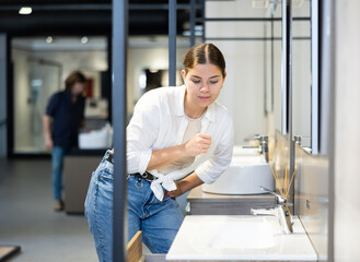 Smiling woman inspects and chooses new kitchen or bath tap faucet at a hardware store