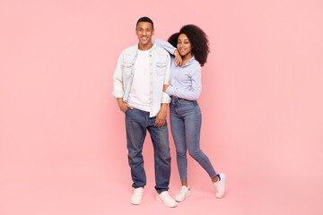 Full length shot of african american couple hugging and smiling at camera, posing on pink studio background, full body length, free space © Home-stock
