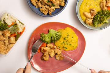 Healthy meal with chicken, manioc, broccoli being eaten by hands with fork and knife in aerial view
