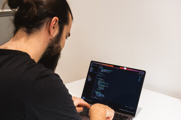 Professional software engineer, IT specialist, programmer, working at home and writing code on a laptop computer. A programmer works remotely at home on his laptop.