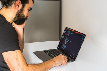 A programmer thinks about how to solve a complex problem. Professional software engineer, IT specialist, working from home and writing code on a laptop computer.