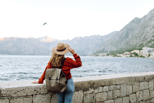 Female traveler in casual sweater taking picture of amazing landscape with mountains, ocean and sunset sky on smartphone during vacation.Tourist during holidays.