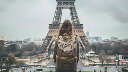 Gordijnen A young female backpacker standing in front of the Eiffel Tower, looking up at the tower, with of her backpack and the city of Paris in the background. © Nawarit