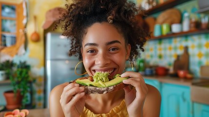 a woman happily eating smashed avocado on toast in a colourful kitchen - obrazy, fototapety, plakaty