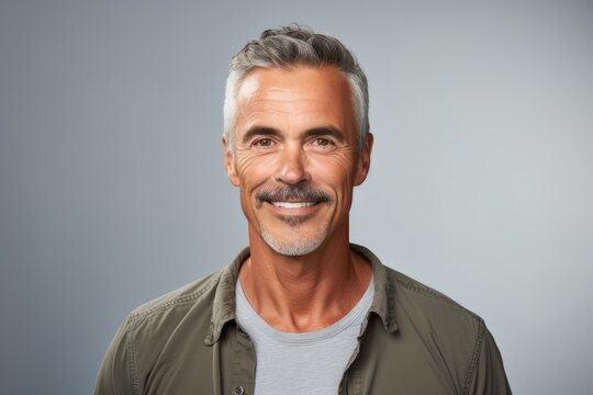 Handsome mature man smiling at the camera while standing against grey background