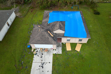 Aerial view of damaged in hurricane Ian house roof covered with blue protective tarp against rain water leaking until replacement of asphalt shingles