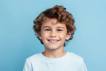 Fotobehang Portrait of a smiling little boy with curly hair on blue background © Iigo